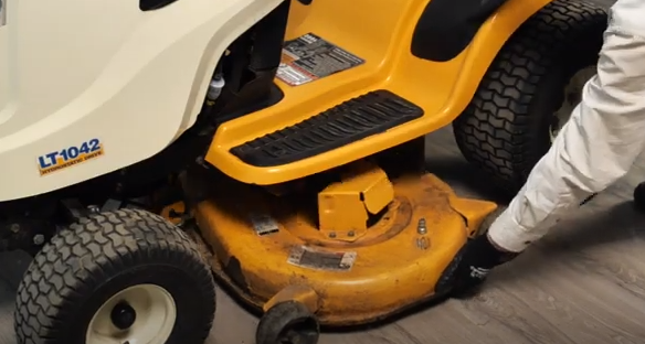 Removing the mower deck from the lawn tractor to access important parts.